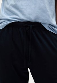 Camiseta de algodón gris superpuesta a pantalones de chándal negros con cordón, que cuentan con una cintura elástica y una textura de tela suave.