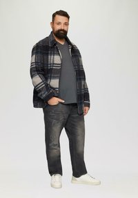 Veste en mélange de laine à carreaux dans les teintes bleu marine, gris et crème, avec un t-shirt gris, un jean noir déchiré et des baskets blanches.