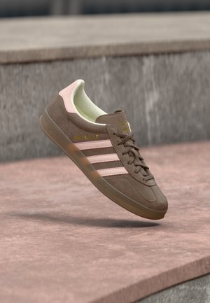 Bruine suède sneaker met roze accenten, drie witte strepen en een geel logo. Voorzien van een zachte voering en een geribbelde rubberen zool.