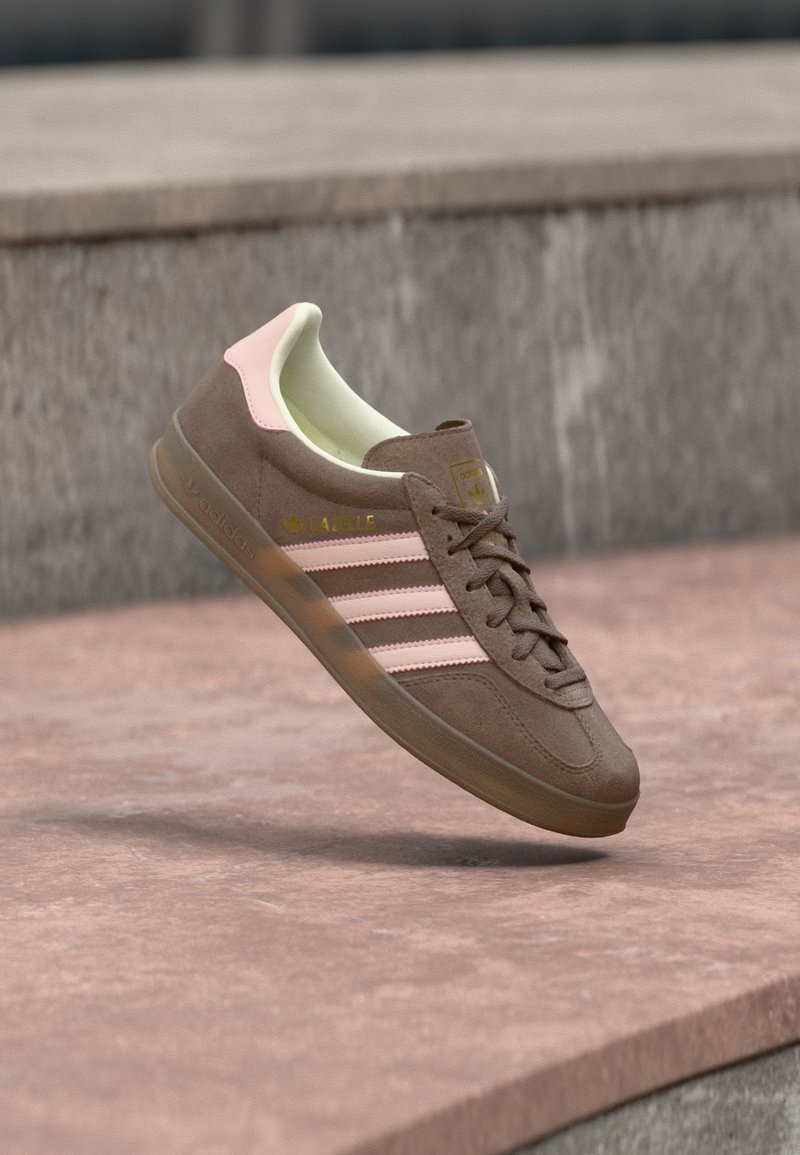 Bruine suède sneaker met roze accenten, drie witte strepen en een geel logo. Voorzien van een zachte voering en een geribbelde rubberen zool.