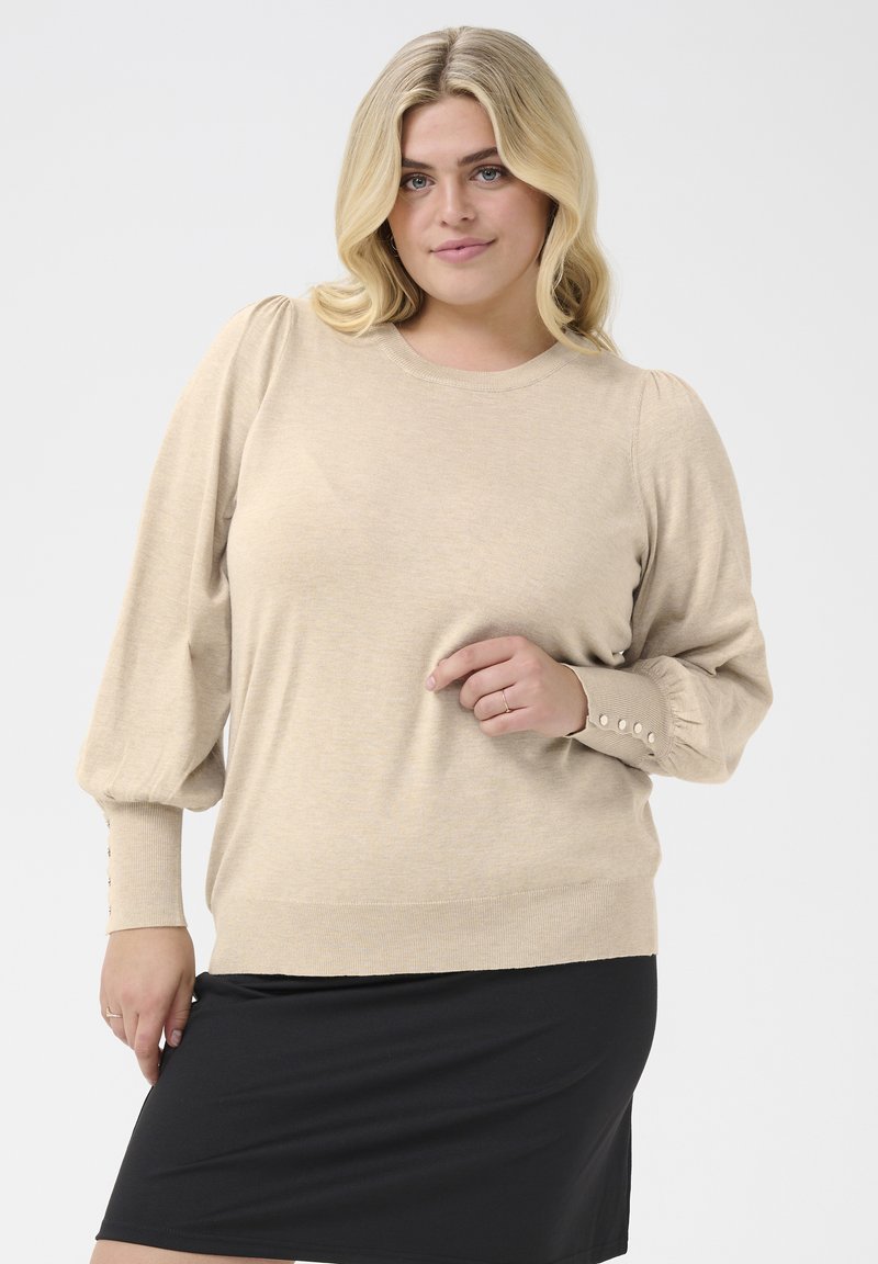 Beige gestrickter Pullover mit Puffärmeln, gerippten Bündchen mit Knopfakzenten, kombiniert mit einem schwarzen Rock. Glatte Textur und lockere Passform.