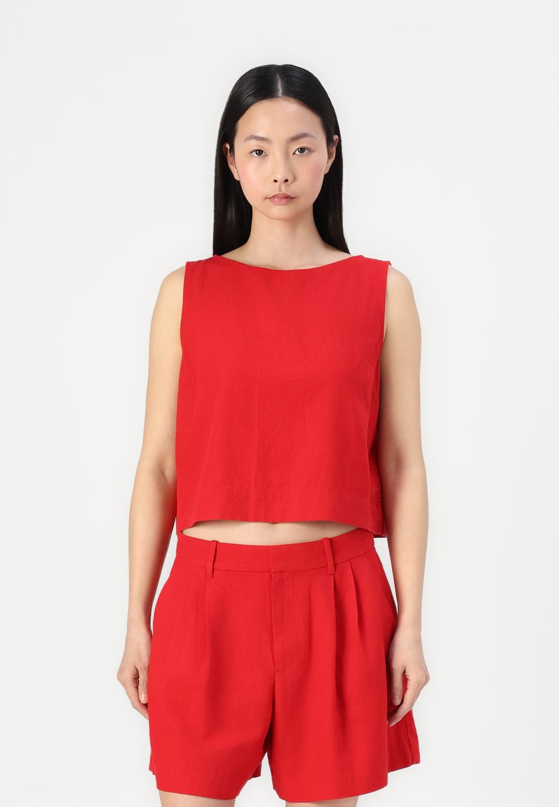 Červený lněný crop top s lodičkovým výstřihem, kombinovaný s červenými šortkami s vysokým pasem a předními záhyby, které mají elegantní střih.