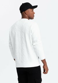 Vit sweatshirt med texturerad logotypdesign, rundad halsringning, långa ärmar och ribbade mudd, tillsammans med svarta cargobyxor.