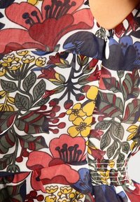 Kwitnąca sukienka z wielokolorowymi wzorami czerwonych, żółtych i niebieskich kwiatów na jasnym tle, z marszczeniami i zapięciem na zamek.