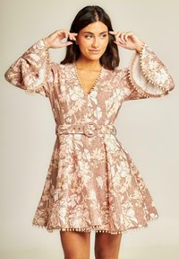 Vestido con estampado floral en rosa claro y beige, con un escote en V profundo, mangas largas de campana y un cinturón con una hebilla decorativa.