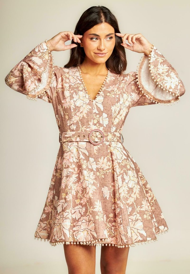 Vestido con estampado floral en rosa claro y beige, con un escote en V profundo, mangas largas de campana y un cinturón con una hebilla decorativa.