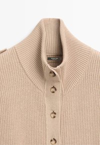 Beige ribbed knit sweater with high collar and five brown buttons down the front, showing a small brand label inside the collar.