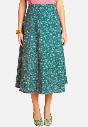 Woman wearing a green midi skirt with pink polka dots, pink top, gold bangles, and green patterned flats, shown from waist to feet.