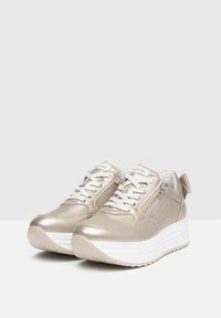 Sneaker metallici oro presentano una texture liscia, lacci bianchi, un accentuato zip sul lato e una suola bianca spessa con un motivo scanalato.