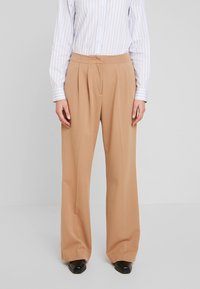 Beżowe spodnie o szerokich nogawkach z zakładkami, wykonane z miękkiego materiału. Połączone z jasnoniebieską, w paski koszulą z guzikiem oraz czarnymi butami.