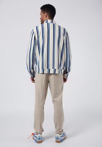 Randig skjorta i kr ämfärgad med blå och svarta ränder; lös passform, långa ärmar och knappmanschetter. Kombinerad med beige byxor och mönstrade sneakers.