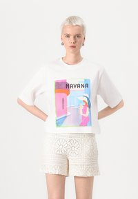 White cotton t-shirt featuring a colorful Havana graphic print, short sleeves, and a relaxed fit, paired with beige lace shorts.