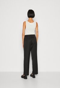 Black wide-leg trousers with a smooth texture, paired with a white sleeveless top. The back view shows a simple design and tailored fit.