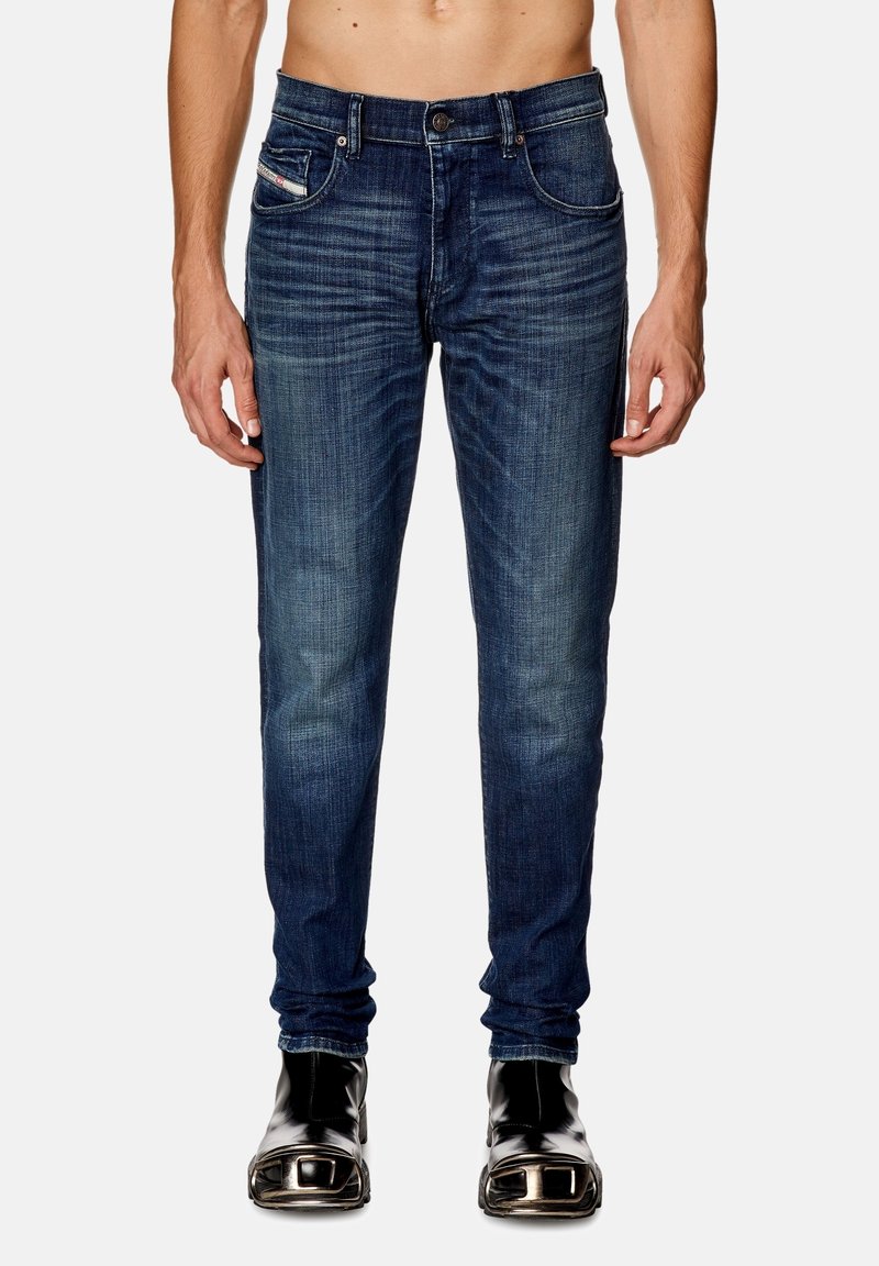 Jean foncé en denim avec une coupe slim, présentant un design classique à cinq poches et un léger dégradé. Associé à des bottines noires à talons brillantes.