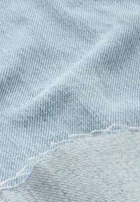 Tejido de mezclilla azul claro con un tejido texturizado; presenta un ligero desvanecimiento y bordes deshilachados. La vista en primer plano enfatiza su suavidad y durabilidad.