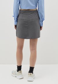 Minifalda gris hecha de tela tejida con una textura suave, que cuenta con dos bolsillos traseros y una cinturilla ajustada. Combinada con zapatillas deportivas.