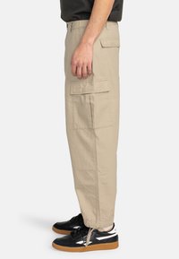 Beige cargo bukser med sidelommer, tapered manchetter og et letstof. Båret med sorte sneakers med hvide detaljer.