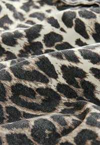 Luipaardprint stof met een gestructureerd oppervlak. Kleuren zijn beige en zwart met contrasterende vlekken. Materiaal lijkt stevig en flexibel te zijn.