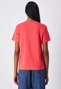 T-shirt a maniche corte e collo rotondo in cotone corallo, con una texture liscia e una vestibilità rilassata, abbinato a pantaloni in denim blu.