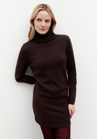 Bruine gebreide coltrui jurk met lange mouwen en geribde manchetten. Licht getailleerd ontwerp, dat boven het midden van de dij valt. Glad textuur.