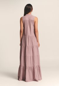 Robe longue à volants rose en tissu texturé. Elle présente un col et un design sans manches, avec un ourlet à volants en bas.