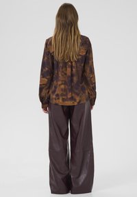 Majica s dolgimi rokavi v rjavem in vijoličnem tie-dye vzorcu, kombinirana s širokimi maroon usnjenimi hlačami. Teksturovana tkanina s sproščenim krojem.