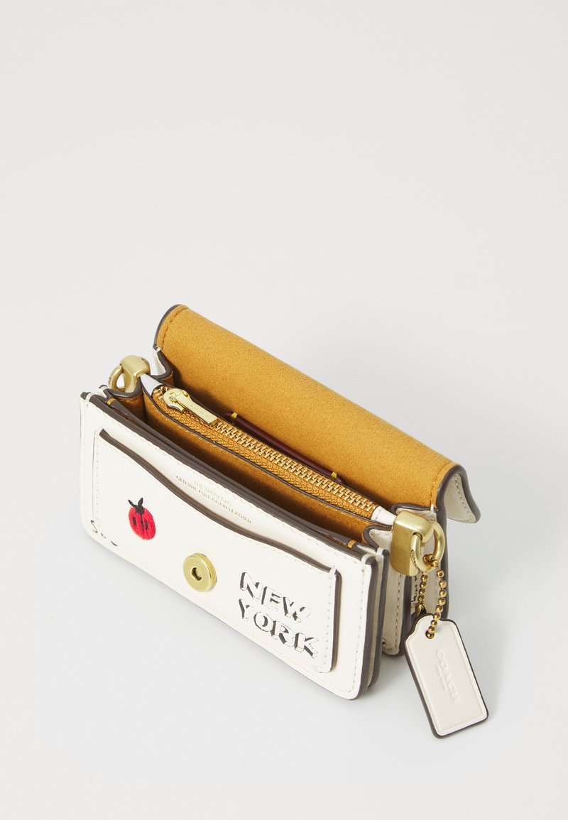 Portefeuille en cuir blanc avec quincaillerie dorée, doublure en daim jaune, inscription "NEW YORK" en relief, et détail coccinelle rouge. Comprend une poche zippée et un porte-clés.