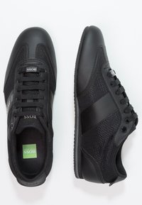 Czarne buty sportowe wykonane z połączenia gładkiej skóry i materiału siateczkowego. Mają zaokrąglony czubek, sznurowany design i teksturowaną gumową podeszwę.