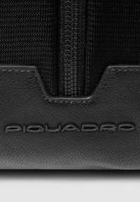 Zwarte leren en gestructureerde stoffen tas met een opvallende ritssluiting en het geperste Piquadro-logo. Strak ontwerp met duurzame materialen.