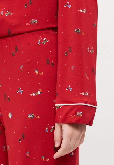 Camisa de pijama vermelha com padrão festivo apresentando pessoas, árvores e animais. Material macio, mangas longas e detalhes em branco nas punhos.