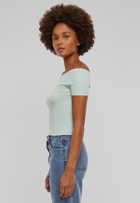 Lys blå av-shoulder topp laget av myk stoff, med korte ermer og et tettsittende design, kombinert med høy midje blå jeans.