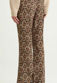 Pantalon évasé marron à motifs présentant des formes ovales superposées en crème, rouille et marron foncé. Tissu lisse avec un design rétro.
