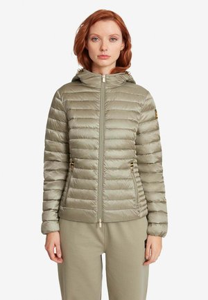 Donna che indossa una giacca trapuntata con cappuccio colore oliva chiaro con cerniera e pantaloni abbinati, in piedi di fronte su sfondo bianco.