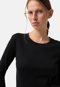 Černý top s dlouhým rukávem, kulatým výstřihem a hladkou strukturou, doplněný o velké obdélníkové brýle s kovovým rámečkem.