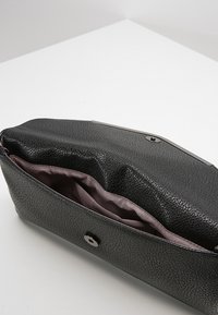 Černé kožené psaníčko s texturovaným povrchem, stříbrným kováním a měkkou fialovou podšívkou uvnitř. Má bezpečné zapínání na knoflík.