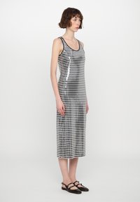 Robe midi rayée argent et noire en matière pailletée, avec un design de débardeur et une coupe droite, accompagnée de chaussures noires.