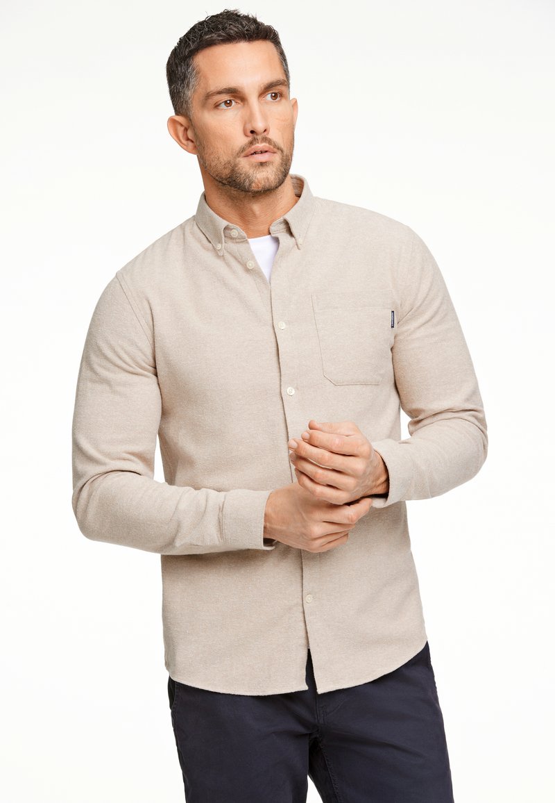 Camicia beige a maniche lunghe con bottoni, dotata di taschino sul petto, realizzata in tessuto strutturato, con un colletto elegante e orlo curvo.