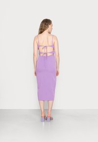 Vestido midi roxo com alças finas, costas abertas com design entrelaçado e laços, textura suave, combinado com sandálias de salto bloco a condizer.