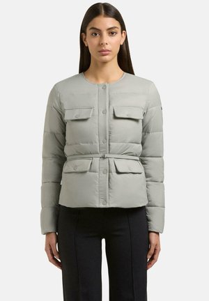 Vrouw draagt een lichtgrijze, doorgestikte jas met ceintuur, drukknopen en vier klepzakken aan de voorkant, gecombineerd met een zwarte broek.