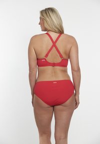 Červený bikiny set s designem křížového zadního dílu, nastavitelnými ramínky a zapínáním na háček. Hladká textura s značkovým akcentem na pase.