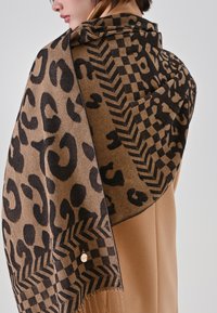 Brauner Schal mit Leopardenmuster, kariertem Design und Zickzack-Akzenten. Leichter Stoff mit Fransenverzierung und einem kleinen Metalletikett.