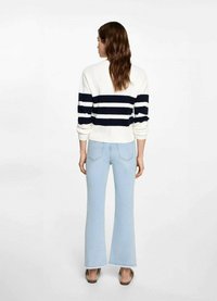 Suéter a rayas blanco y marino con textura acanalada; combinado con jeans acampanados de color azul claro. El conjunto se completa con sandalias marrones.
