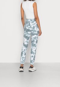 Světle modré a bílé joggers s tie-dye vzorem, s tapered střihem, spárované s bílým ribbed crop topem a teniskami s černými akcenty.