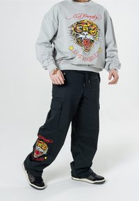 Šedá mikina s potiskem tygra a červeným nápisem, spárovaná s černými cargo kalhotami se stejným designem tygra. Černé tenisky dotvářejí outfit.