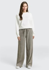 Witte trui met lange mouwen in een ontspannen pasvorm, gecombineerd met lichtbruine wijde broek met een gestructureerd patroon en verstelbare trekkoord.