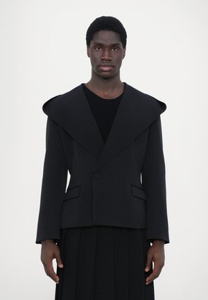 Schwarze, maßgeschneiderte Jacke mit breiten Revers, einreihiger Knopfverschluss und zwei Fronttaschen. Glatte Textur, strukturierter Schnitt und taillierte Silhouette.