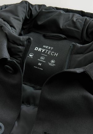 Sort jakke med en glat, mat overflade og en nylonforing, mærket "NEXT DRYTECH," str. M. Inkluderer fleeceforede lommer.