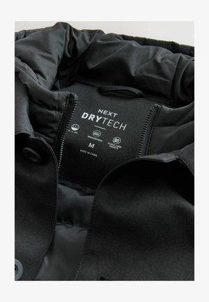 Veste noire avec un extérieur lisse et mat, doublée en nylon, étiquetée "NEXT DRYTECH," taille M. Comprend des poches doublées en polaire.