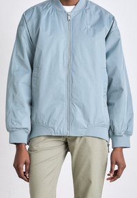 Světle modrá bomber bunda se zipem vpředu, žebrovanými manžetami a pasem. Na hrudi malý logo CK. Měkký, hladký materiál.