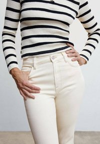 Jeans blancos de cintura alta con una textura suave, que cuentan con un diseño clásico de cinco bolsillos y sutiles detalles de costura. Combinados con un suéter de canalé a rayas en blanco y negro.